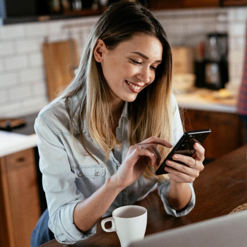 Person smiling and looking at their cell phone. They are happy because they just received their real estate floor plans from Clickapro