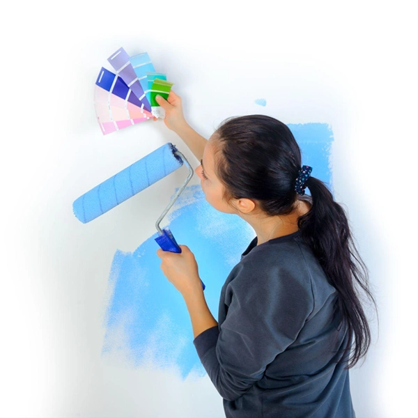 A woman is painting her wall. She is holding up color samples trying to figure out which color to use. She is using Clickapro's 'Inches to Square Feet' home improvement calculator to determine how much paint she needs.